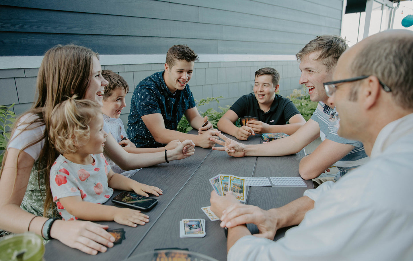 Landscape Photo of Family Playing a Game of Cards from Grandpa Beck's Games on a Grey Table 